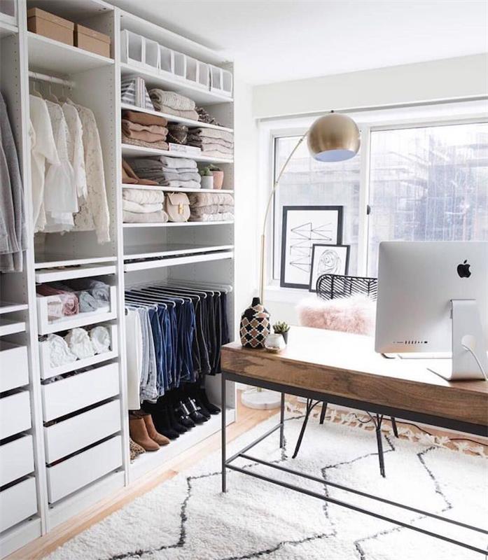 Sovrum med träbord i skandinavisk stil och mac -dator för arbete, vit matta med geometriska former, garderob utan dörrar, öppen klädförvaring