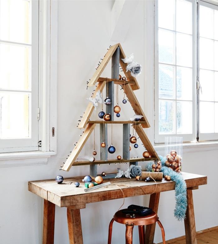drevený strom vyrobený z kúskov paliet, oranžových a modrých ozdobných vianočných gúľ, taburetky s medeným povrchom, modrej girlandy