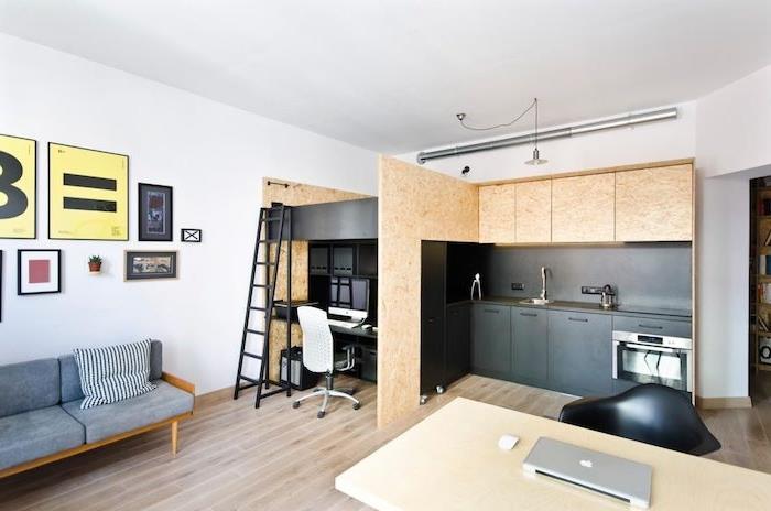 Skandinavisk stil av svart och trä kök med skrivbord bredvid och sovplats ovanför sovrummet, som vetter mot minimalistiskt designat vardagsrum