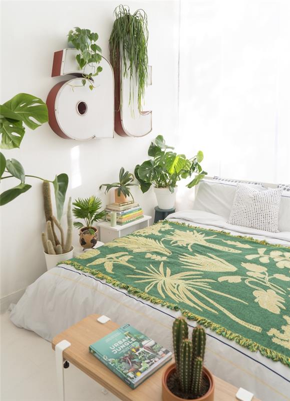 moderná výzdoba spálne pre dospelých v bielej posteľnej bielizni a zelenej posteľnej prikrývke, biele dekoratívne písmená so zelenými akcentmi a ďalšie kvetináče s exotickými rastlinami
