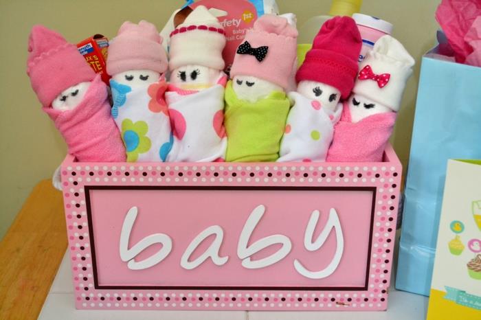 krabička pre tehotnú ženu v ružovej farbe s iniciálkami bielymi písmenami Dieťa, dievčatko, bábätko, navinuté ponožky, aby vytvorili malé deti