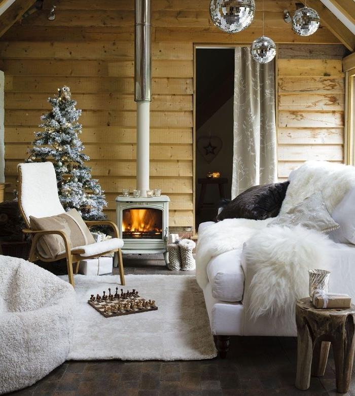 biela pohovka biely koberec a kreslo drevená stolička rustikálny krb drevená stena a vianočný stromček zdobené rustikálnym elegantným dekorom