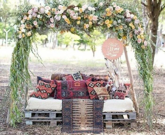 soffa-i-pall-dekorerad-med-kuddar-orientalisk-stil-under-en-blommig-altare-dekoration-paletter-bohem-chic-bröllop