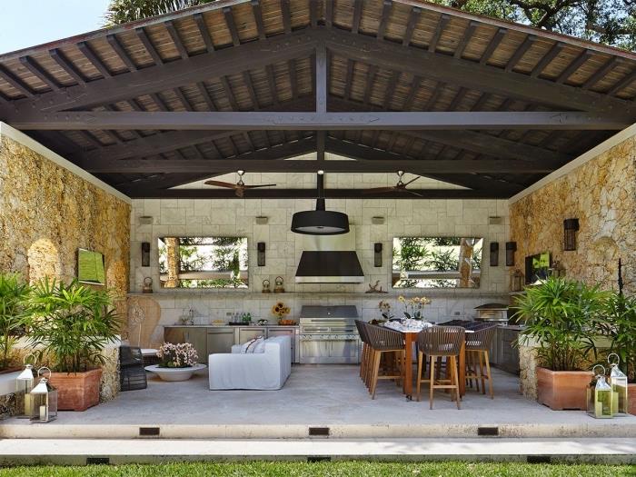 vzorová kuchyňa v záhrade s tmavou strechou z masívu a kamennými stenami, záhradný nábytok s bielou sedačkou