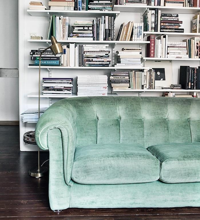 celadonová zelená pohovka v škandinávskej obývačke s bielou knižnicou s niekoľkými policami na pozadí a hnedými parketami