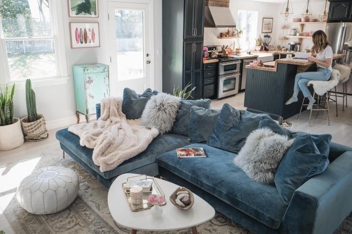 en stor mysig soffa i ankblått sammet som sitter mitt i ett bohemiskt elegant vardagsrum som är öppet mot köket