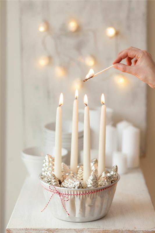 Vianočná dekorácia, aby ste si to uľahčili, s bielymi sviečkami a ozdobnými šiškami, umiestnenými v bielej keramickej miske, ozdobené jemnou červenou a bielou šnúrkou okolo