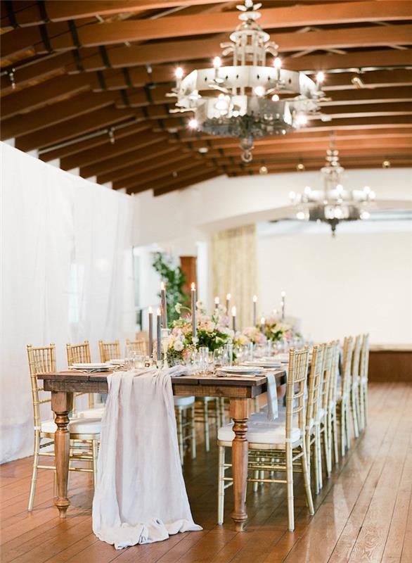 odhalené trámy a priemyselné lustre v svadobnej sieni obloženej bohémami so stolom zo surového dreva a bežcom na stôl, ozdobnými sviečkami, svadobnou témou z industriálneho vinobrania