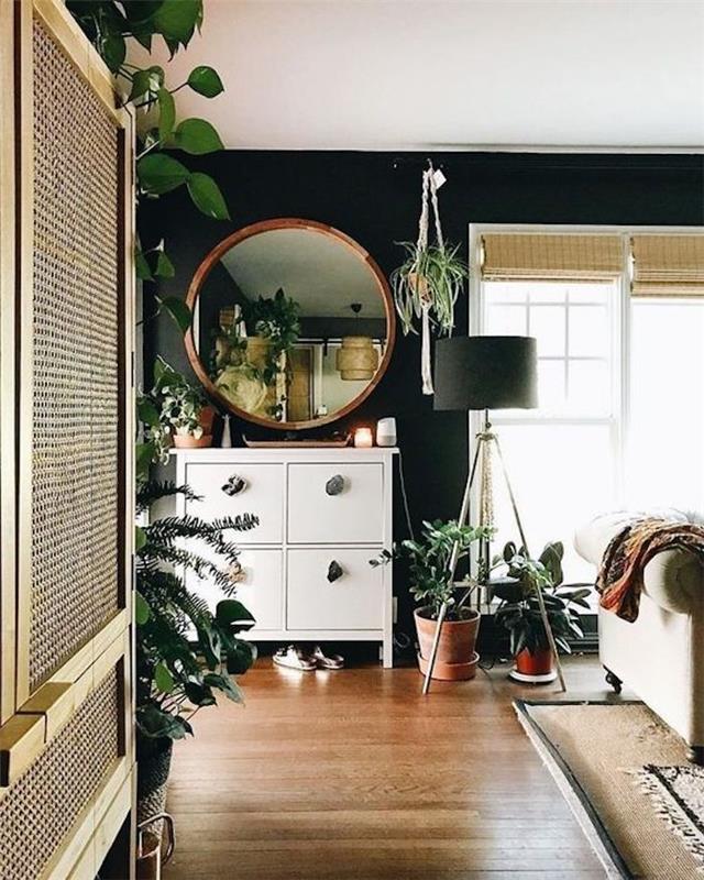 Moderný interiér v miestnosti s množstvom zelených rastlín, okrúhle zrkadlo, trojnohá lampa, béžová sedačka, žalúzie koberec, obývačka s tmavomodrými stenami