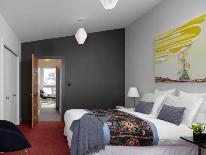 غرفة نوم أحادية اللون ، سجادة حمراء ، كرسي أسود ، جدار رمادي فحمي ، لوحة تجريدية ، منقوشة عرقية