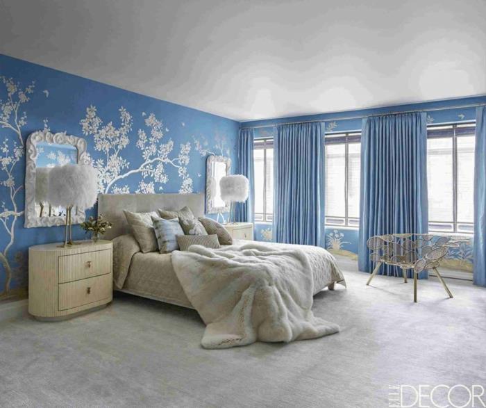 غرفة نوم للبالغين مغمورة باللونين الأزرق والأبيض ، وخزائن أدراج صغيرة بيضاء بجانب السرير ، ومصابيح من الريش ، وسجاد رمادي ، ومرايا بيضاء
