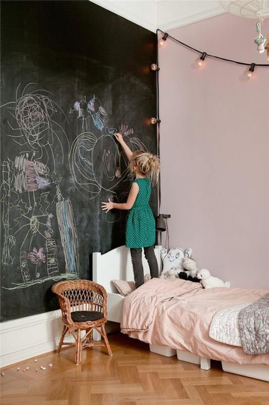 dekorácia spálne pre dospelých s tabuľou na celej stene na kreslenie a písanie, nástenná dekorácia so svetelnými girlandami v tvare žiaroviek, nízka posteľ v bielej farbe, s malým kreslom v tkanej palici vedľa postele
