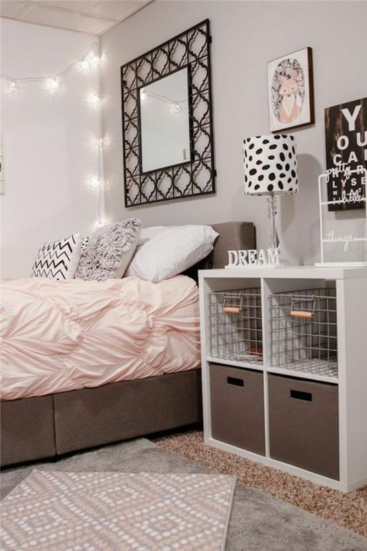 dekorácia spálne pre dospelých veľká posteľ s ružovou dekou a kovaným zrkadlom v štvorcovom tvare, nízka biela skrinka s kovovými úložnými boxmi