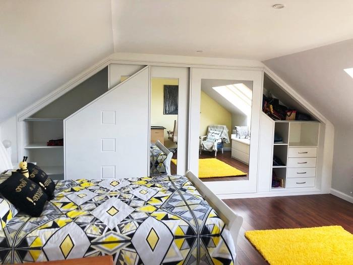 ett vitt vindsrum med gula och grå detaljer med en skräddarsydd sluttande garderob