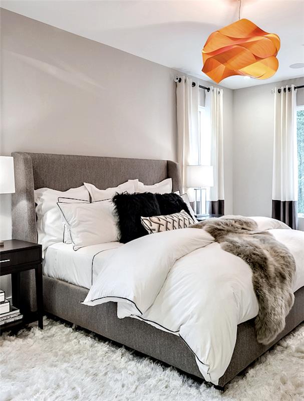 príklad sivobielej spálne, osvieženej oranžovým akcentom, závesné svetlo v štýle origami, mäkký koberec, sivá posteľ, prikryté bielou bielizňou