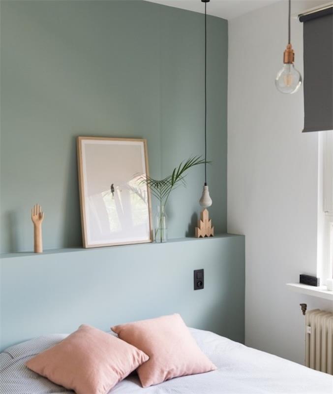 Škandinávska spálňa so stenami premaľovaná na zelenú farbu Celadonského odtieňa, biela posteľná bielizeň s malými čiernymi pruhmi, ružové vankúše, originálne zavesenie
