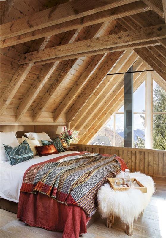 Podkrovná šikmá spálňa v rustikálnom štýle s teplými prikrývkami na konci postele pokrytá parketami zo svetlého dreva z ovčej kože