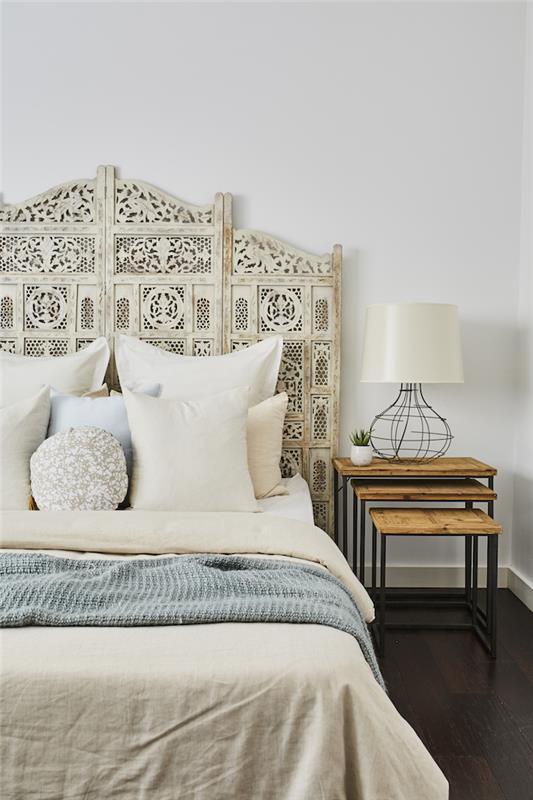 spálňa v bohémskom štýle biela čelo postele biele vankúše béžová a modrá pokrýva nočný stolík v drevenej a kovovej bielej stene