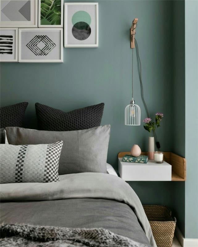tmavosivé zelené steny v dizajnérskej spálni pre dospelých, sivá a čierna posteľná bielizeň, drevený nočný stolík, pripevnený k stene, stena z ozdobných rámov pri čele