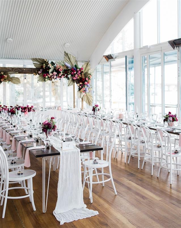 girlandy a kytice z ružových a červených kvetov v bielej svadobnej miestnosti so svetlými parketami, behúňom na bielom plátne, klasickými nápadmi na svadobnú výzdobu