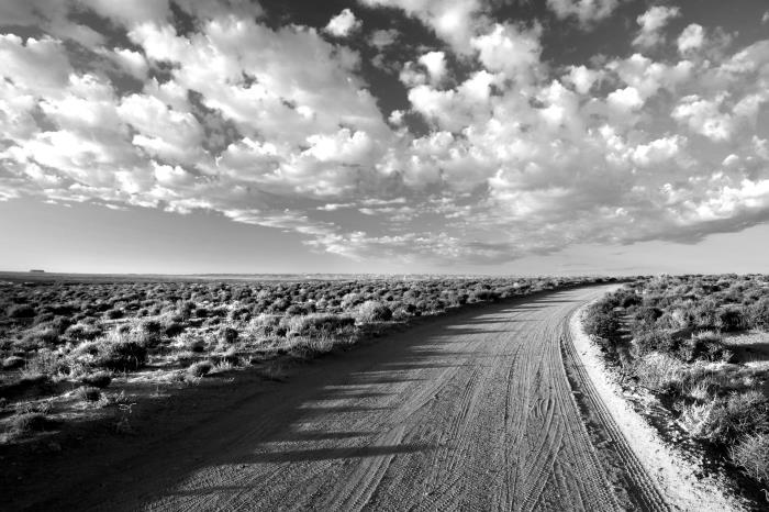 svartvitt fotografi av en stig i öknen som går vilse i horisonten, under skådespelet av de dansande molnen
