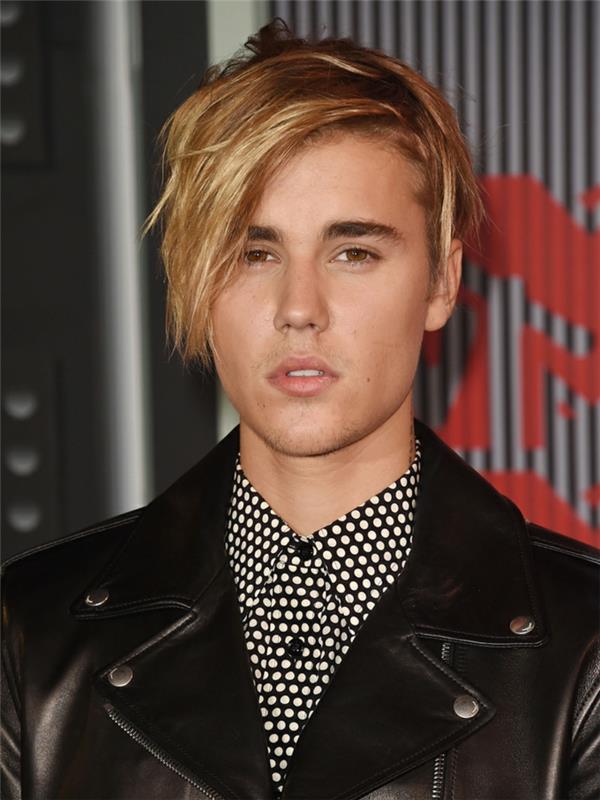 Justin Bieber moderného strihu, blonďavé vlasy, bočná ofina, bodkovaná košeľa, čierna bunda