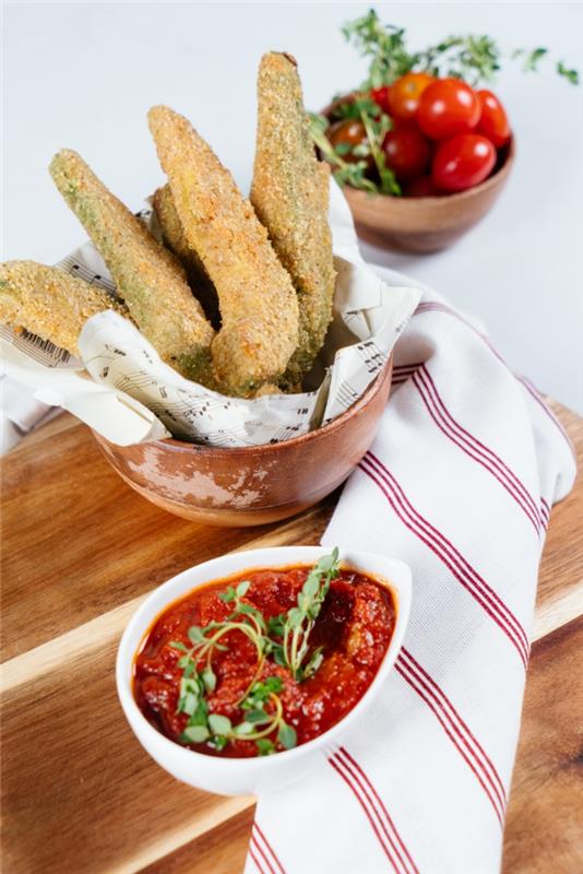 skärbräda i trä, tomatsås och körsbärstomater i små skålar, recept på fingermat, avokado -pommes frites