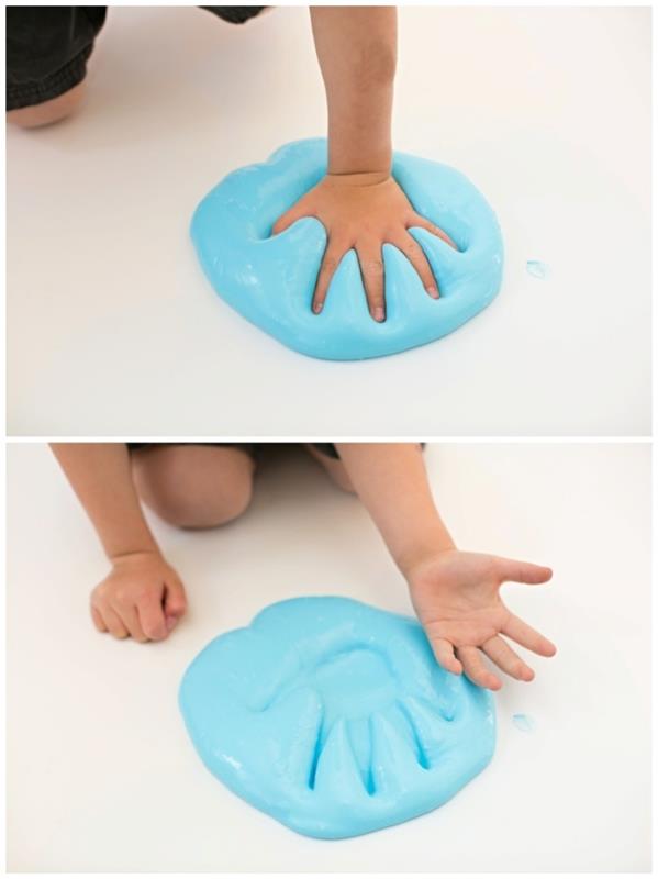 طفل صغير يضغط على يده أو يده ، في كومة كبيرة من الوحل الأزرق الرقيق ، يوضع على سطح أو أرضية ناعمة بيضاء