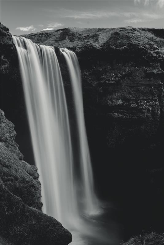 en vacker svartvit bild majestätiskt vattenfall i berget som belyser dess vatten