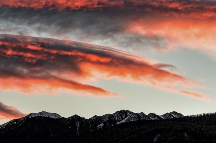 vulkaniskt landskap i svart och rött, himmelska landskap, himmel i orange och svart mot en bakgrund av klarblå himmel, silhuetter av bergstoppar