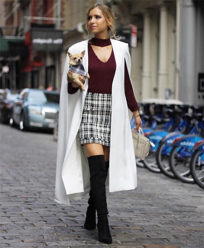 امرأة تمشي في الشارع مع chihuahua ، توقعات اتجاهات الموضة لعام 2019 ، ترتدي تنورة منقوشة ومعطف أبيض طويل ، أحذية عالية للركبة