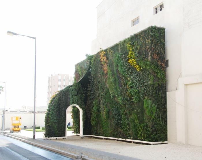 vonkajšia zelená stena s oblúkom s bielymi dverami, inštalácia v zelenej, žltej a hnedej farbe, vertikálne pestovanie, doplnkový prvok budovy s bielymi stenami