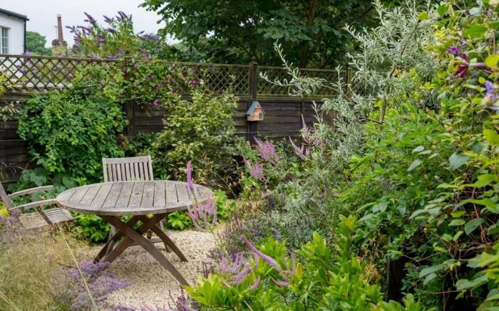 príklad malej záhrady s kamienkami a zelenými rastlinami, ktorá má priestor na odpočinok pri stole a drevené skladacie stoličky