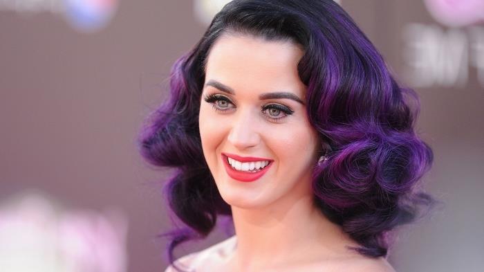 Katy Perry med lila hårfärg, axellång lockig frisyr med svarta rötter och lila spetsar