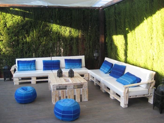 paletový záhradný nábytok bielené paletové pohovky s bielymi podsedákmi a ozdobnými vankúšmi a modrými pohovkami, konferenčný stolík z paliet, zelená stena
