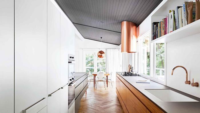 nápad, ako usporiadať kuchyňu na dĺžku s drevenou kuchynskou skrinkou a bielou policou, svetlými parketami, jedálňou v drevenom stole a modernými stoličkami, vysávačom a medeným závesným svetlom