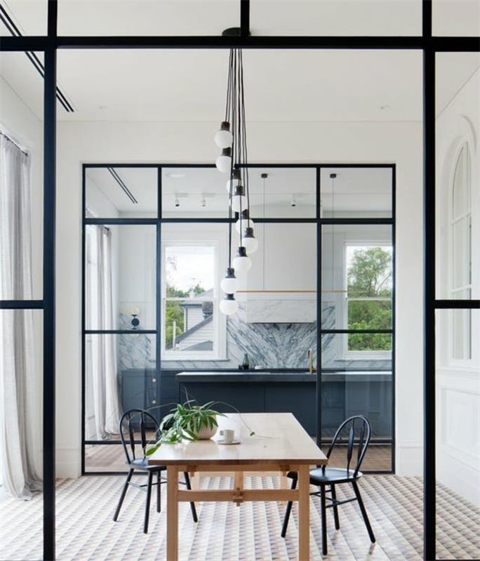antracitovo šedá otvorená kuchyňa s mramorovým efektom a bielou skrinkou, oddelenie čiernou sklenenou strechou, drevený stôl a čierne kovové stoličky, mozaiková podlahová krytina s geometrickými vzormi, závesné svetlo s žiarovkou