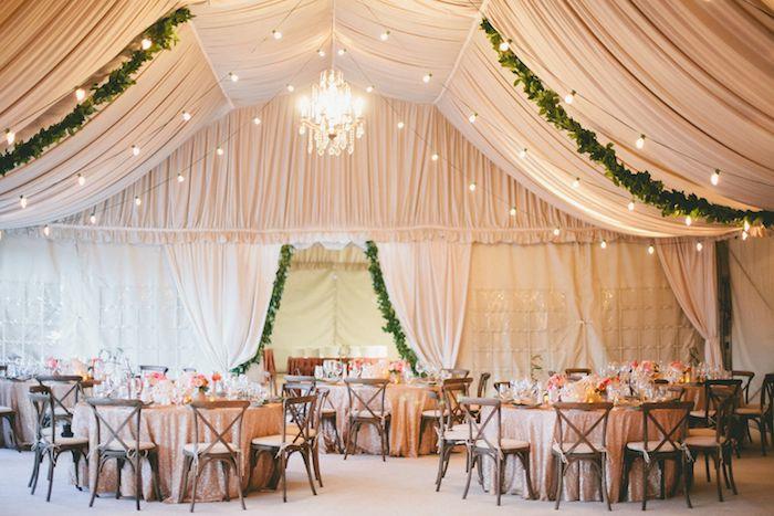 svadobná stropná výzdoba z béžových závojov, svetlej girlandy a elegantného lustra, drevené stoličky okolo stola zdobené ružovým obrusom
