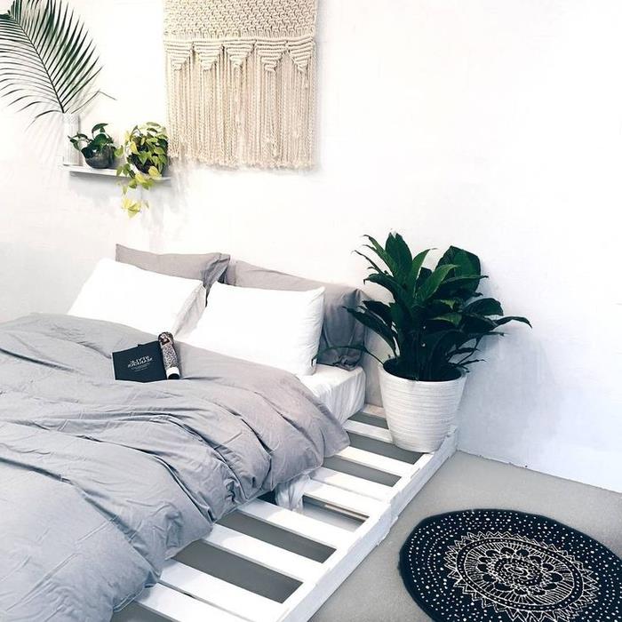 biela a sivá spálňa s bohémskou elegantnou atmosférou s jednoduchou posteľou z paletového boxu presahujúcou matrac