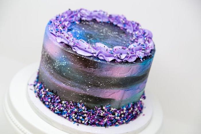jednoduchá narodeninová torta pre dospelých s purpurovou a čiernou polevou a ozdobou z maslového krému na vrchu, ozdobou modrej a fialovej gule a posypom