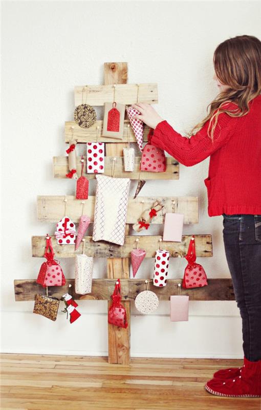 drevená jedľa vyrobená zo skrížených dosiek, ozdôb a darčekov zabalených v červeno -bielom ozdobnom papieri, biele darčeky s červenými bodkami