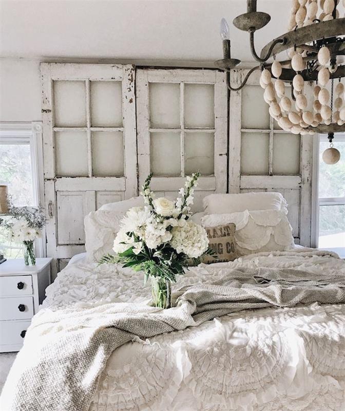 återvunna trädörrar rå utseende med vita sängkläder och grå pläd, bukett vita blommor, elegant ljuskrona, country chic stil