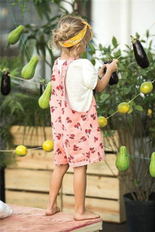 byxor ser ut, liten flicka, rosa hängsel med frukt, vit t-shirt, gult pannband
