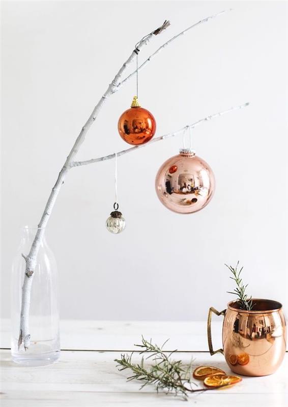 biela vetva v plastovej fľaši ozdobená vianočnými guľami rôznej veľkosti, medeným pohárom, rozmarínom, sušenými plátkami pomaranča