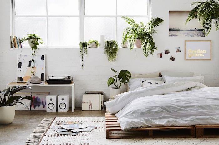 Paletová posteľ v bielej spálni v severskom štýle s množstvom zelených rastlín a vinylových platní
