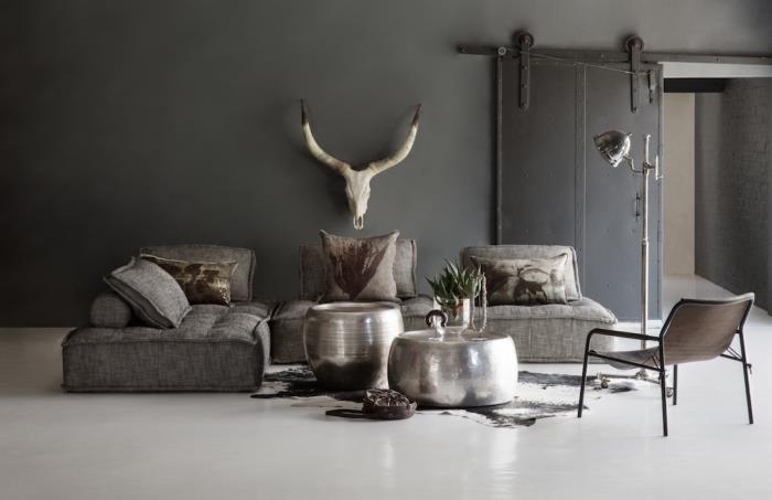 rustik atmosfär i ett stort vardagsrum med mörkgrå väggar och vitt golv med mörk hörnsoffa och imiterad djurtäckmatta