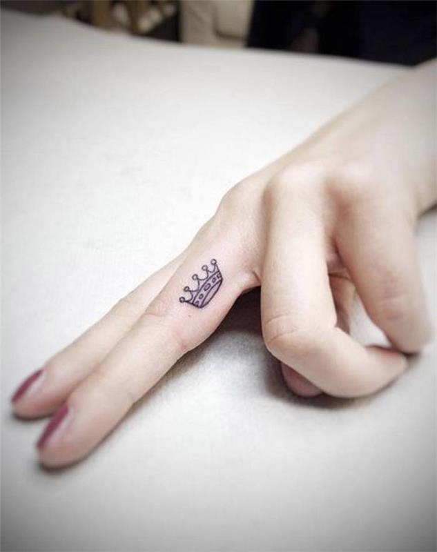 Tatuaggi piccoli mani e un'idea con una corona sul dito medio di una donna