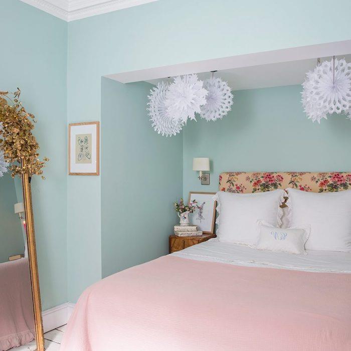 Pastelovo modrá farba na spálňu pre dospelých a práškovo ružová prikrývka na posteľ, čelo postele s kvetinovým vzorom, zrkadlo s retro dizajnom, dekorácia papierovou vločkou