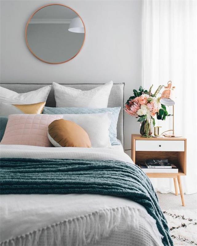 pärlgrått sovrum med rund spegel ovanför sängen med blåaktiga kuddar