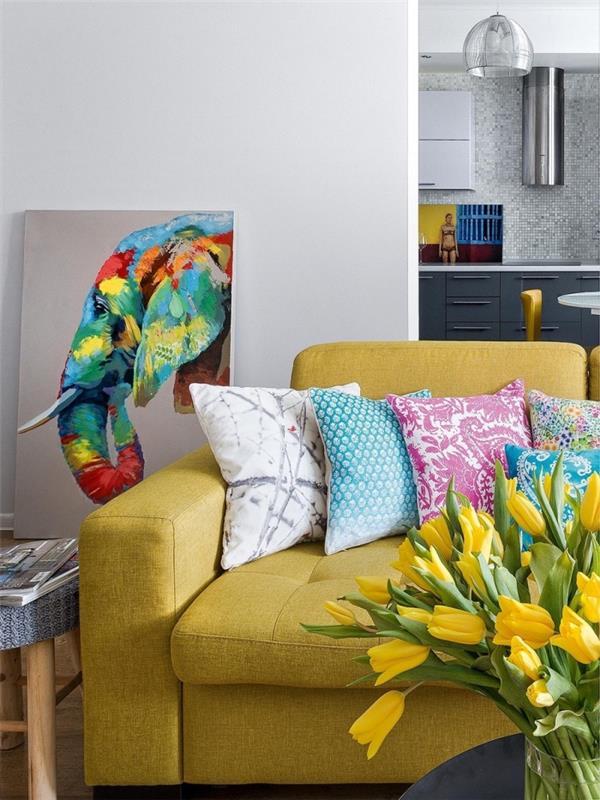 honosné akcenty v svetlošedej obývačke, model sedačky z horčicovožltej farby prikrytý farebnými vankúšmi s etnickými vzormi